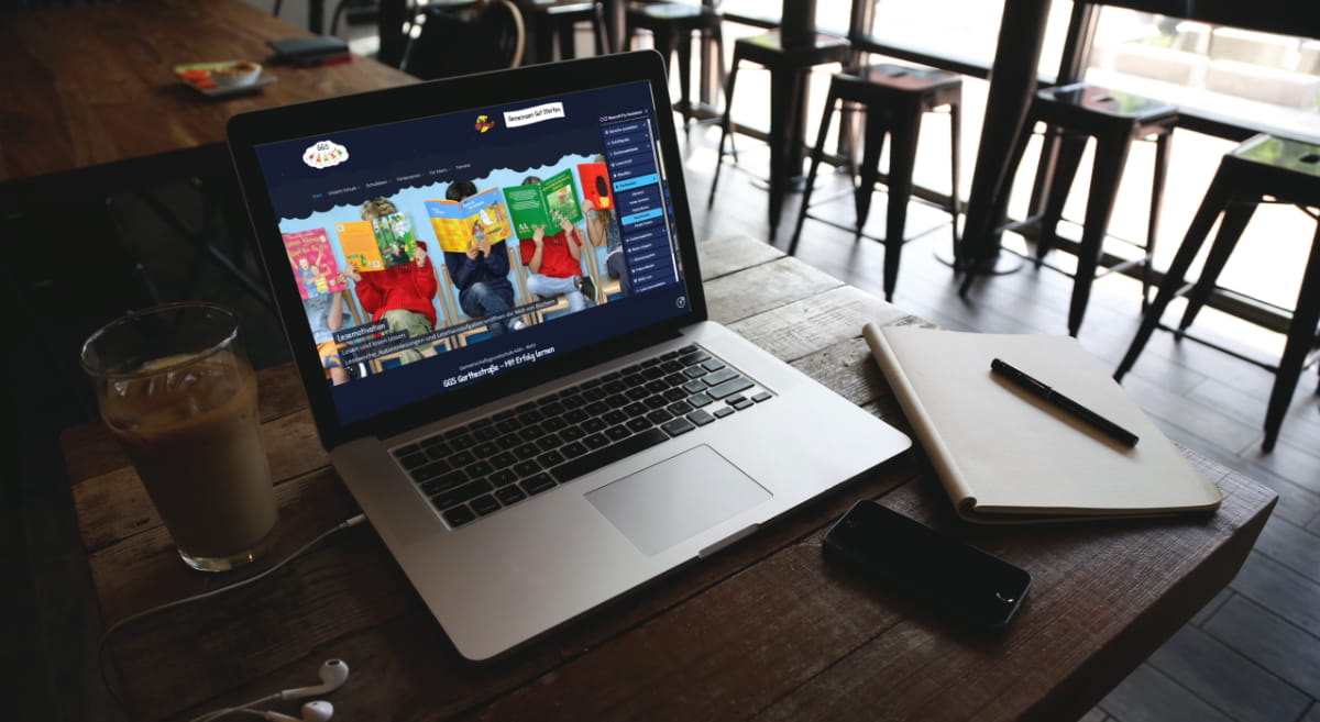 Auf einem Laptop in einem Café ist die Webseite der GGS Garthestraße zu sehen, in welcher der NeuroA11y Assistenten benutzt wird